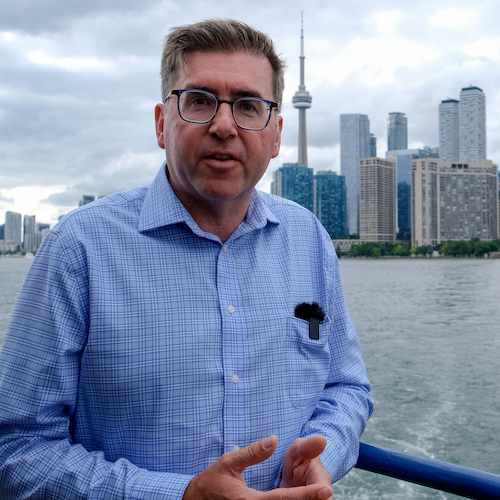 Dr. Brian Doucet on a boat with the Toronto skyline behind him.