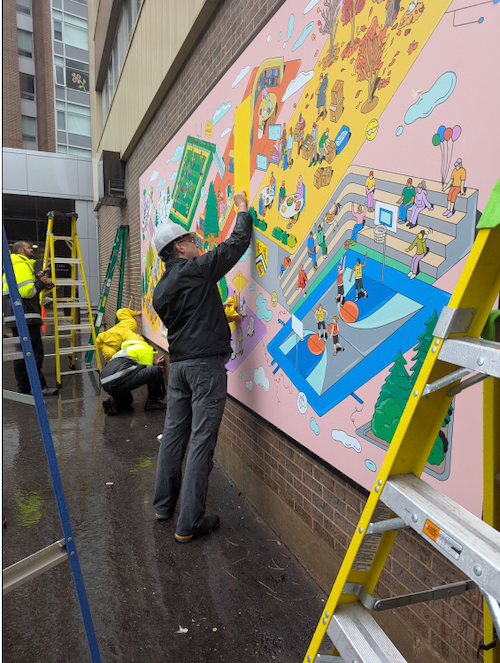 Workers install the mural on the exterior wall.