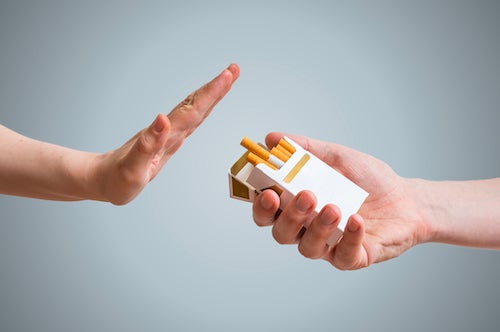 A person holds up a hand to stop another from offering a cigarette from a pack.