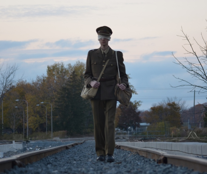 Sam Beuerle, a central character in the play, walks in his Army uniform along the railway tracks, his eyes bandaged.