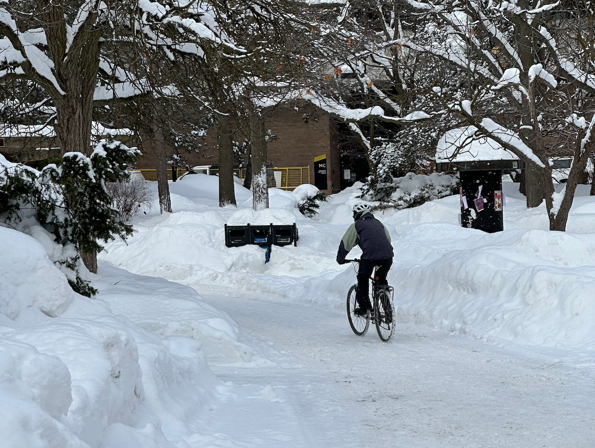 A cyclist bikes on a snow-covered path through campus during winter.