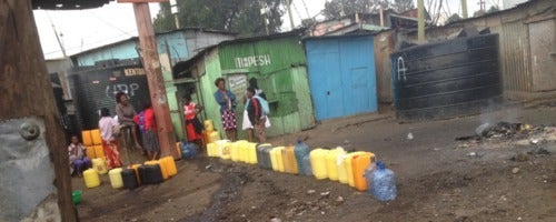 Women stand near a collection of water jugs.