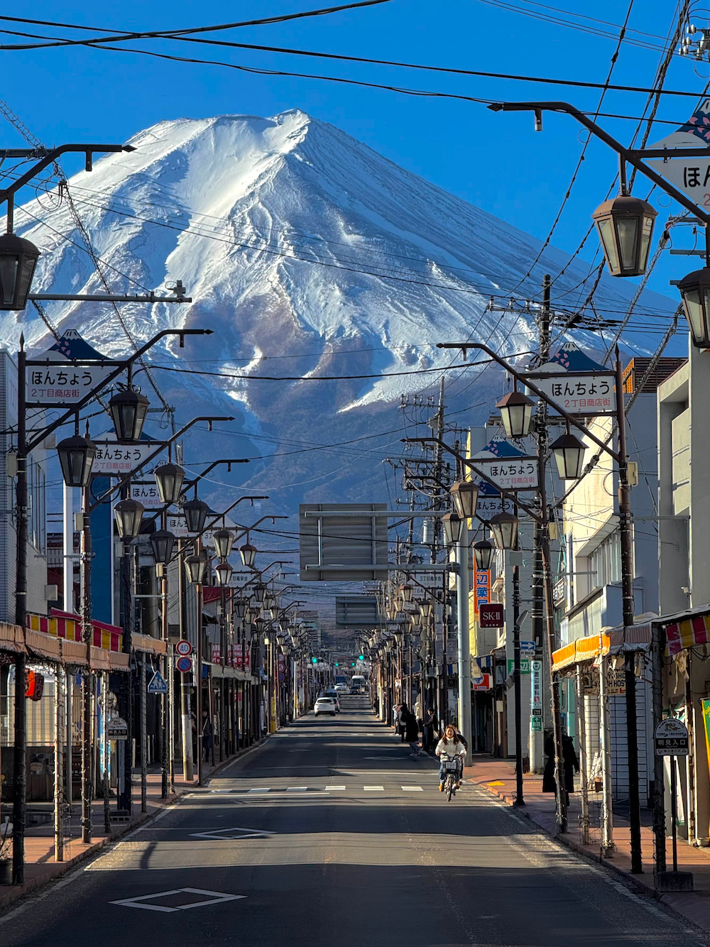 A snow-covered mountain seen from a street lined with shops and street lights in Kawaguchiko, Japan.