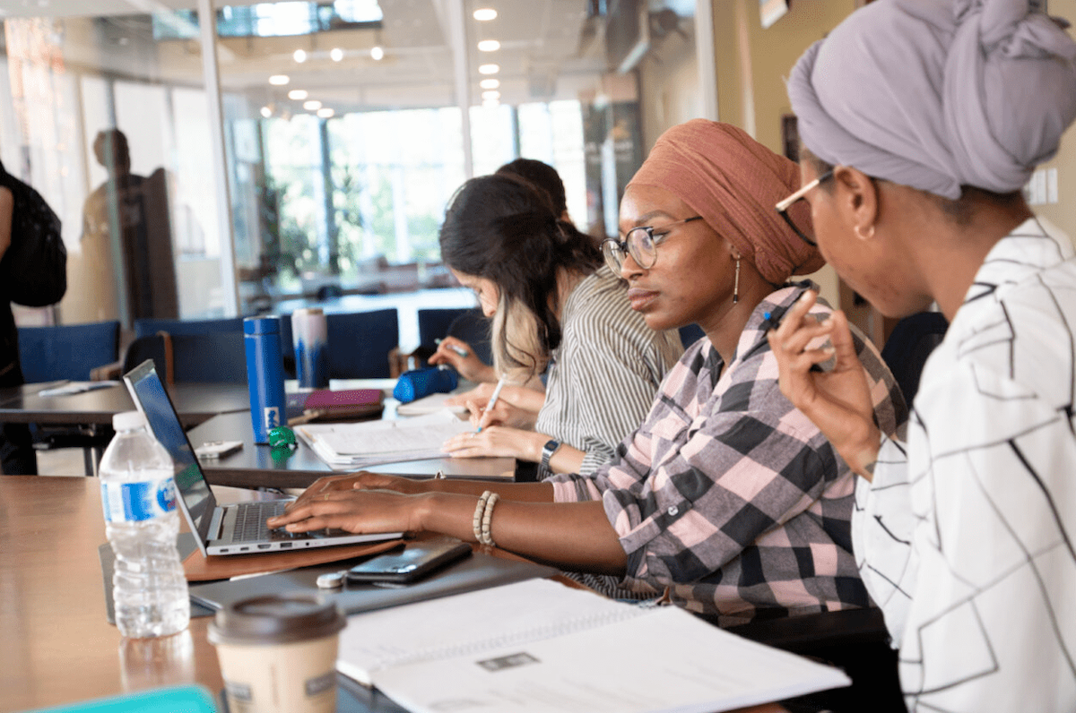 Several graduate students seated at a table with laptops.