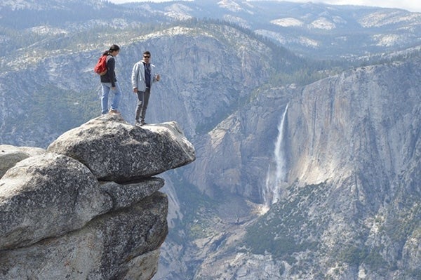 Two people stand on a cliff in Yosemite National Park.