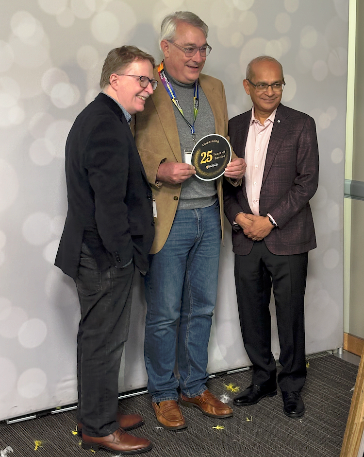 Professor Jim Rush holds his 25-year placard as James Skidmore and Vivek Goel stand with him.