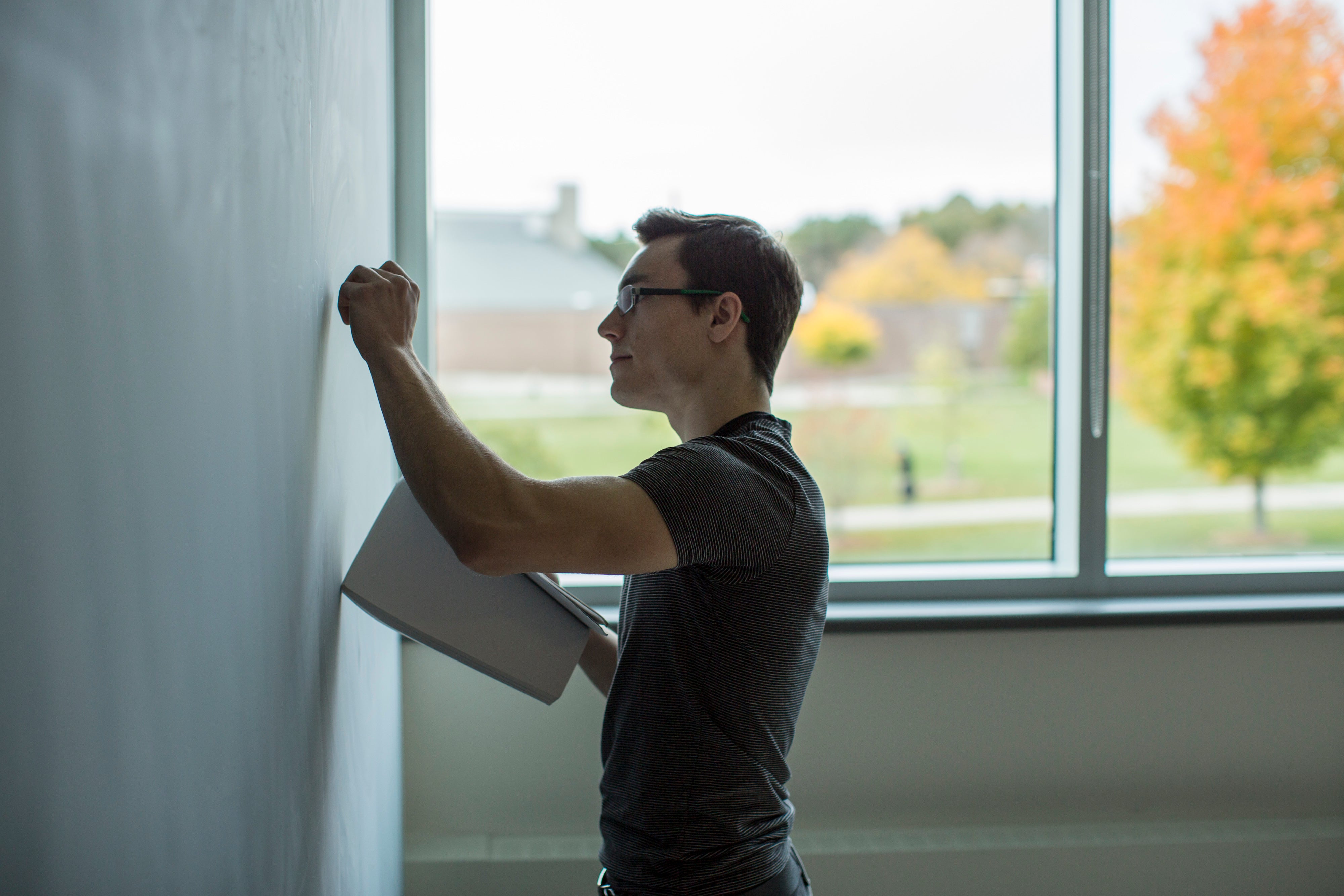 A man standing and writing at a black chalkboard.
