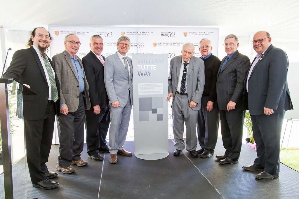 Waterloo Mathematics representatives stand with the William Tutte Way signpost.