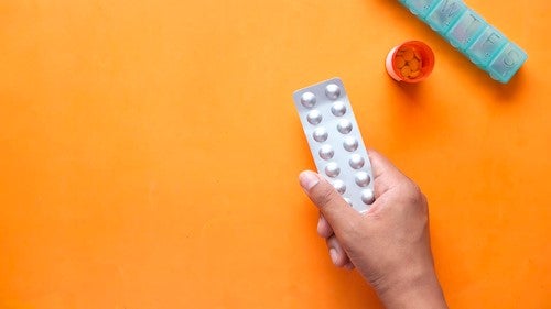 A person holds a pill packet with a bottle nearby