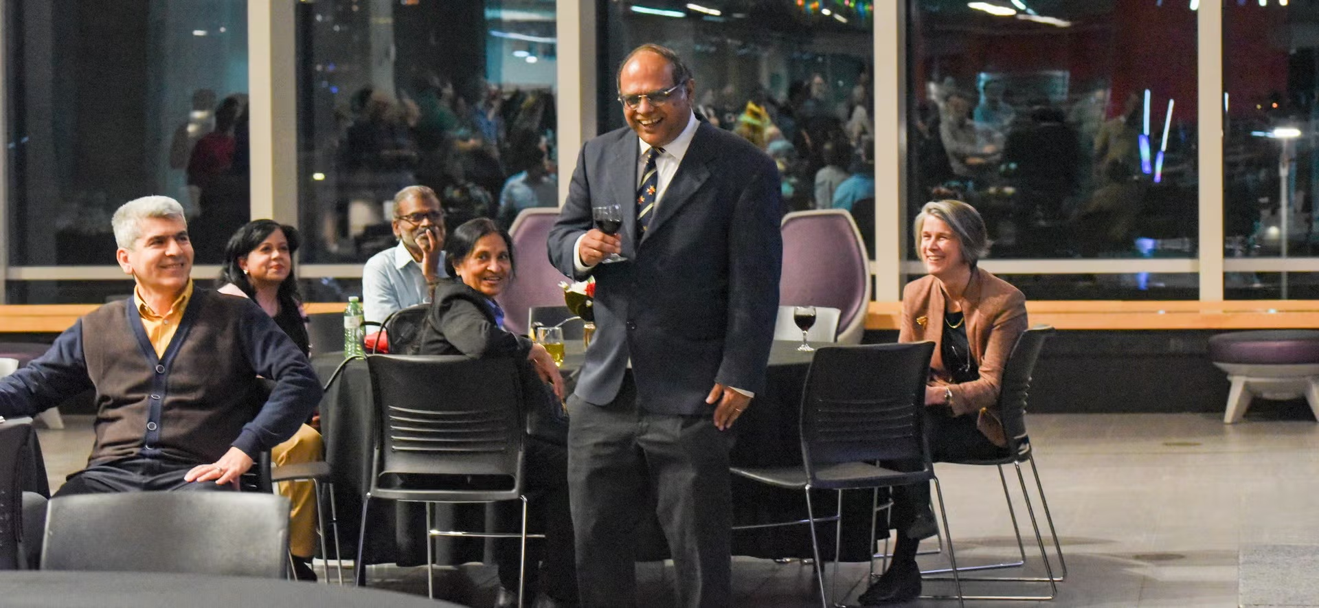 Dr. Kumaraswamy Ponnambalam, glass of wine in hand, stands as he is celebrated at his retirement party.