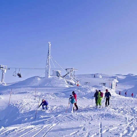 Skiers get off a chairlift at the top of a ski hill.