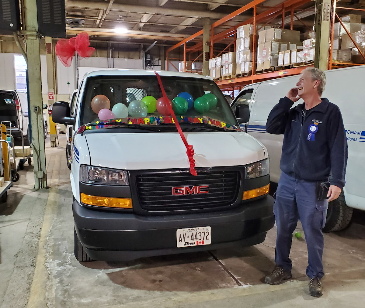 Bill Coram laughs as he looks at his delivery van decorated with birthday ribbons and balloons.