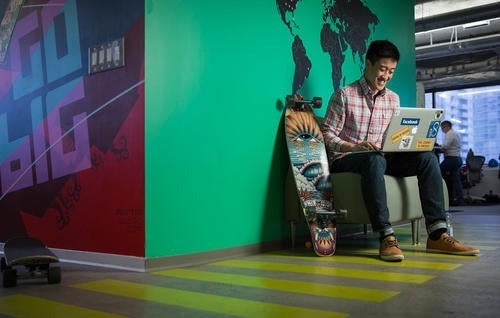 A man sits next to a skateboard while reading a laptop.