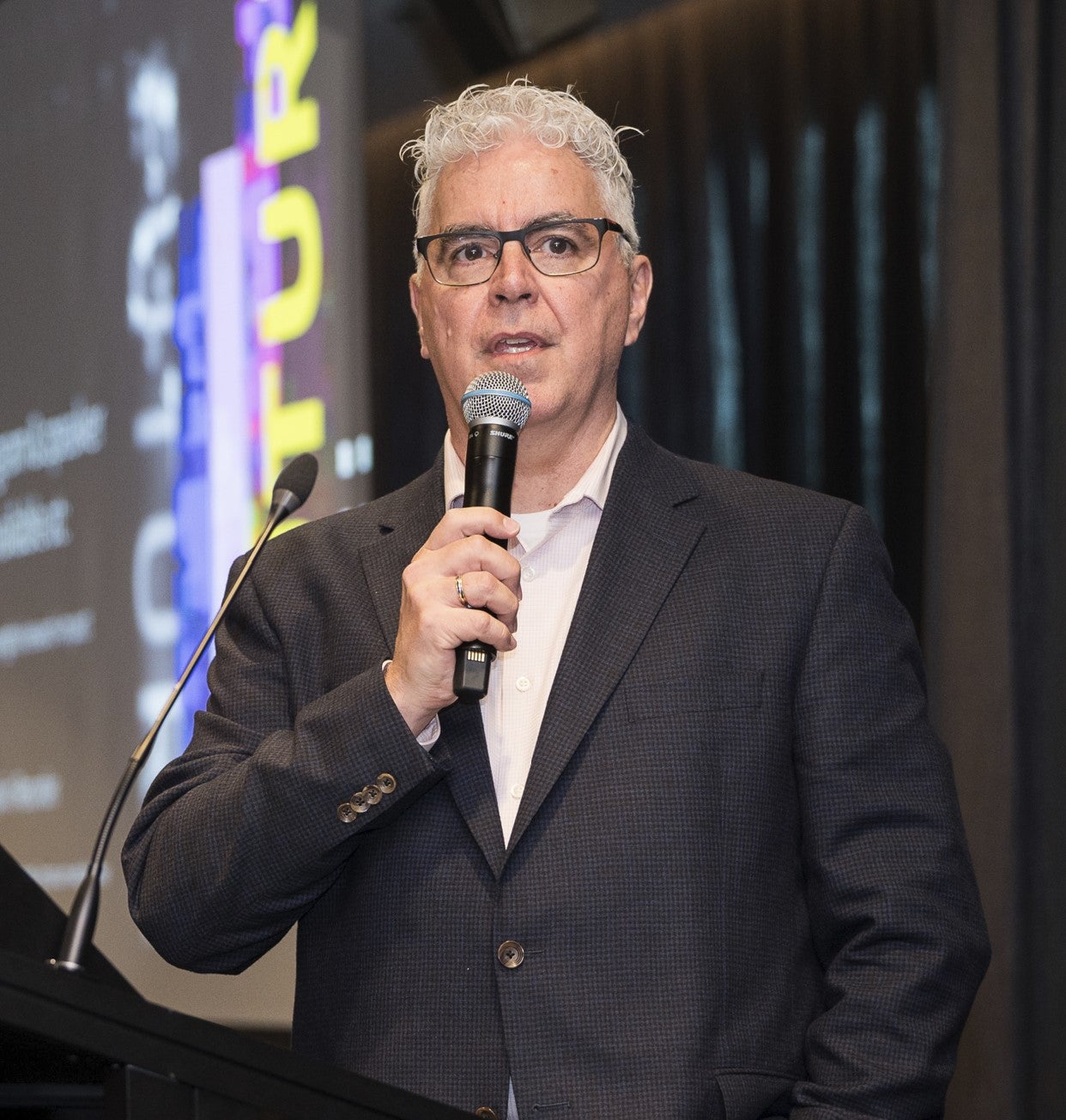 David Phipps stands on a stage speaking into a handheld microphone during a presentation.