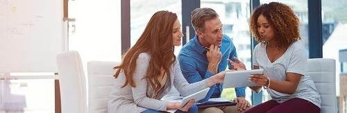 three coworkers in discussion over a tablet screen