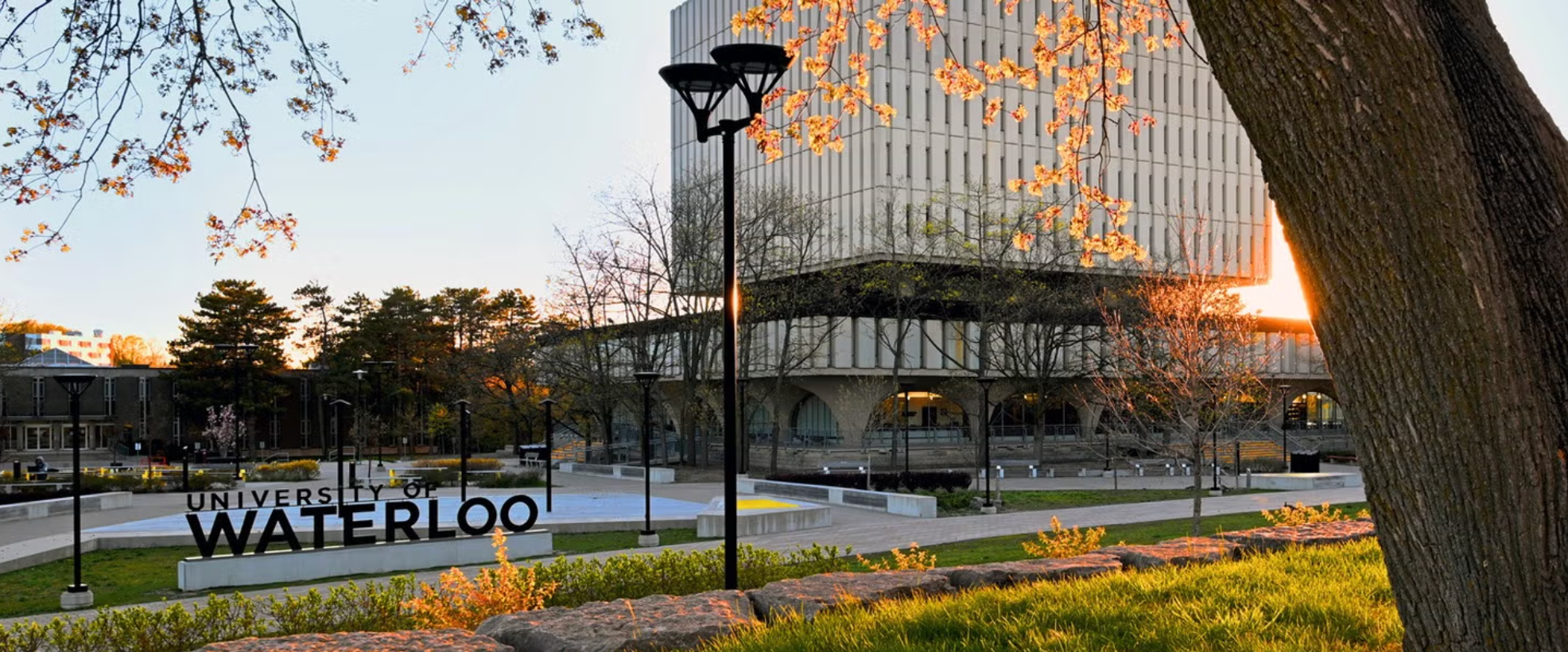 University of Waterloo campus with the Waterloo sign and surrounding buildings at sunset.