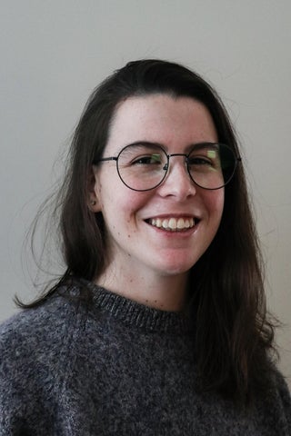 photo of Kat Webster wearing grey sweater, glasses, and smiling directly at camera