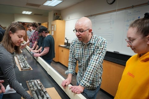 A professor chats with students over mineral samples in a lab. 