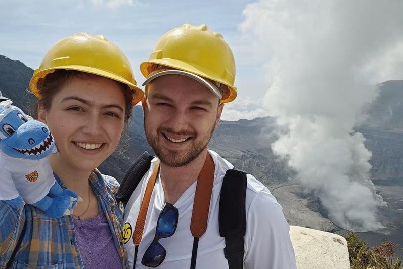 A male and female student pose with a stuffed Cobalt toy with mountains in the background.