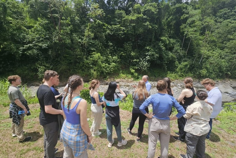 A group of students stand on the edge of a river. 