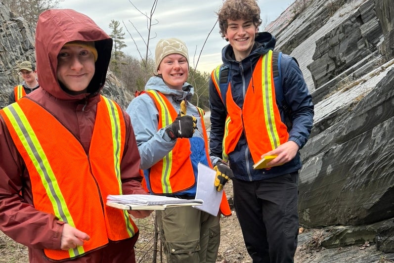 Three students next to a rock formation. 