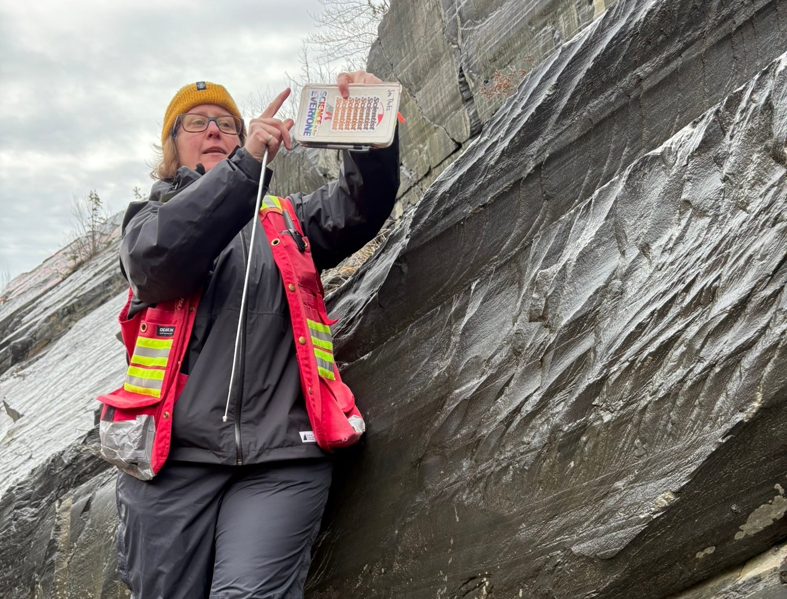 A woman in an orange vest standing in front of a rock formation. 