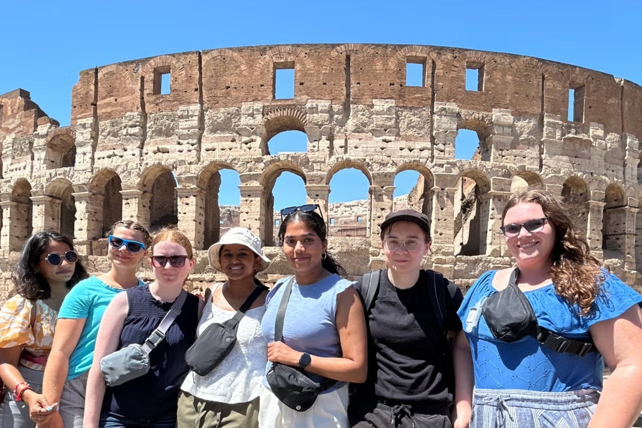 A group of female students pose in a line in front of the Colosseum in Rome.