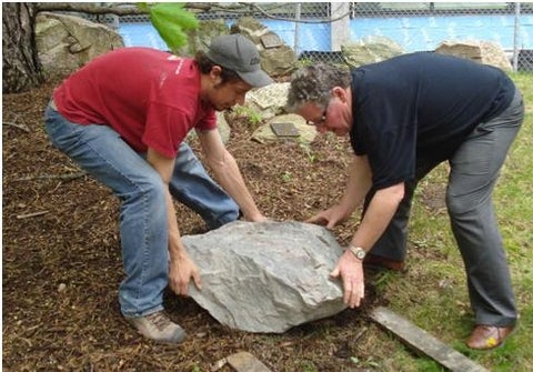 The 600 lb (272 kg) boulder being placed in the Peter Russell Rock Garden by two of the donors.