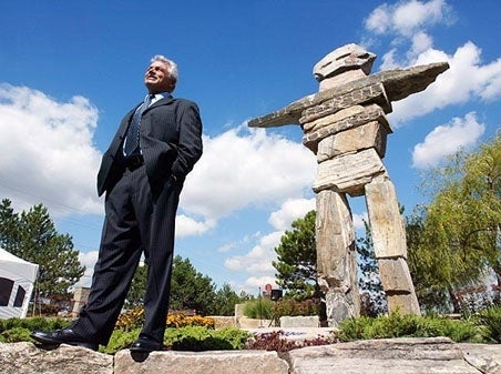 A man standing in front of the largest inukshuk in the world.