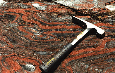 red and black bands seen on flat rock surface with geologic hammer resting on top