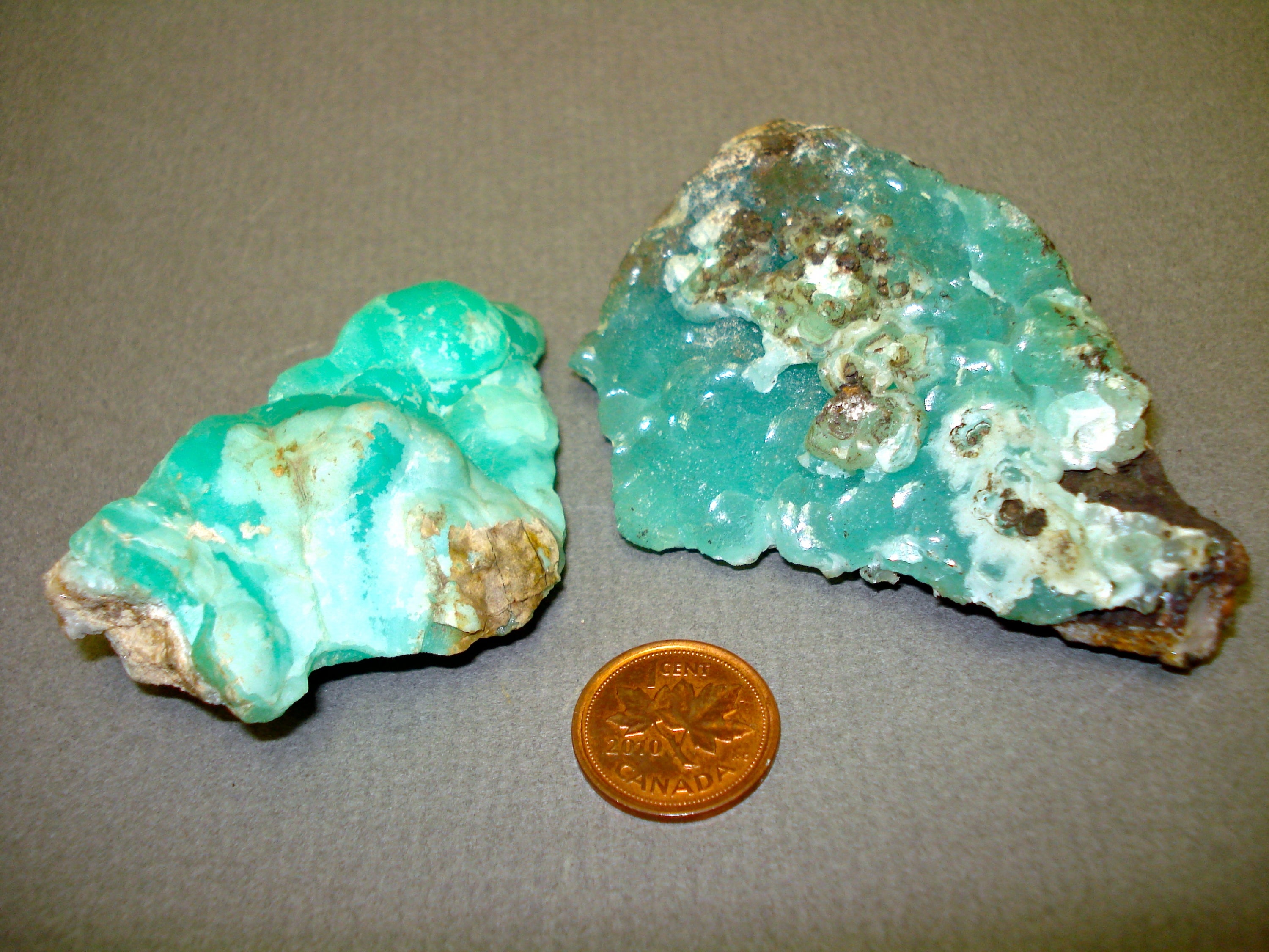 a couple of pieces of smithsonite next to a penny for size comparison