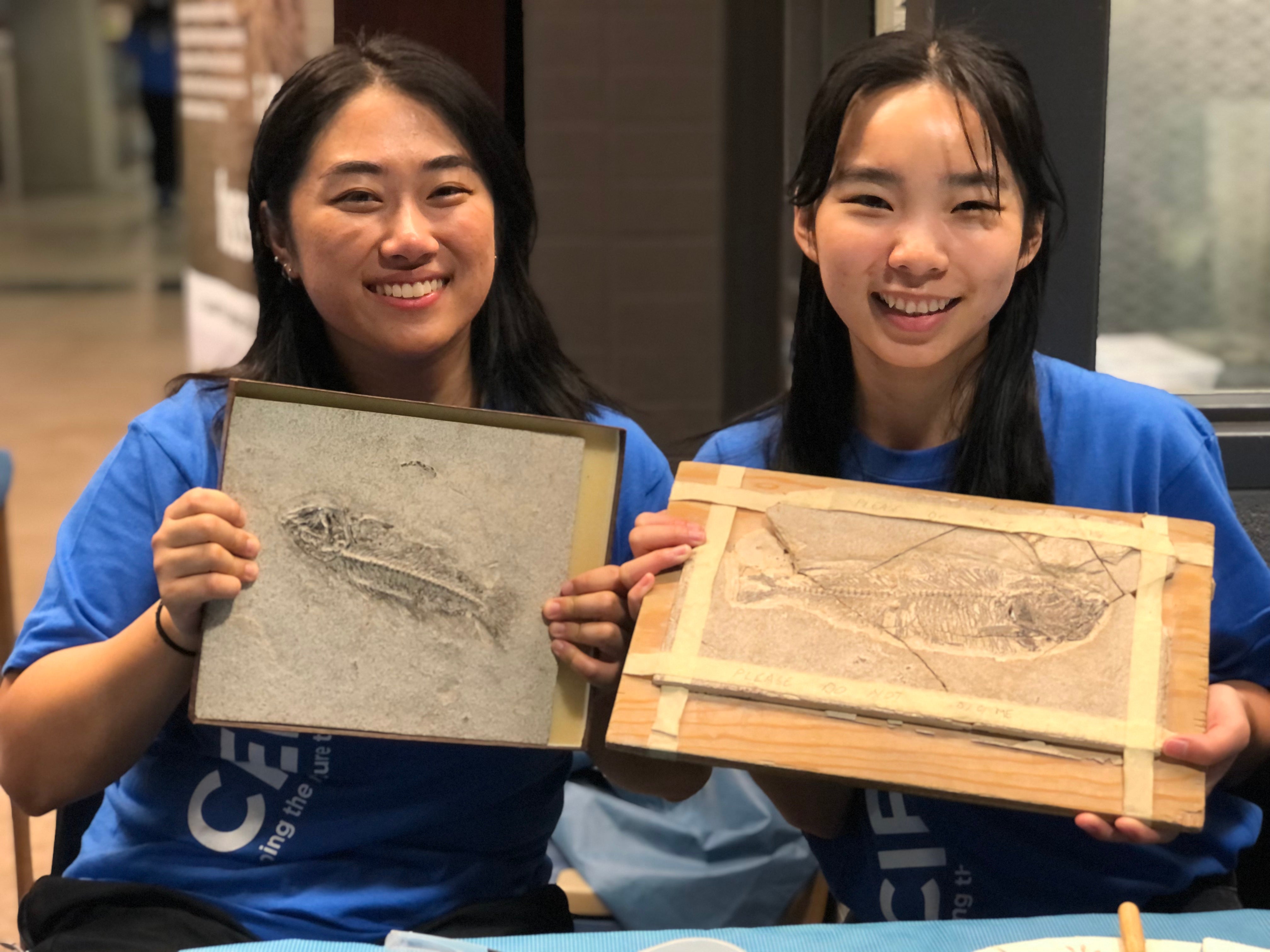 Two girls holding up plaques displaying fossil fish 