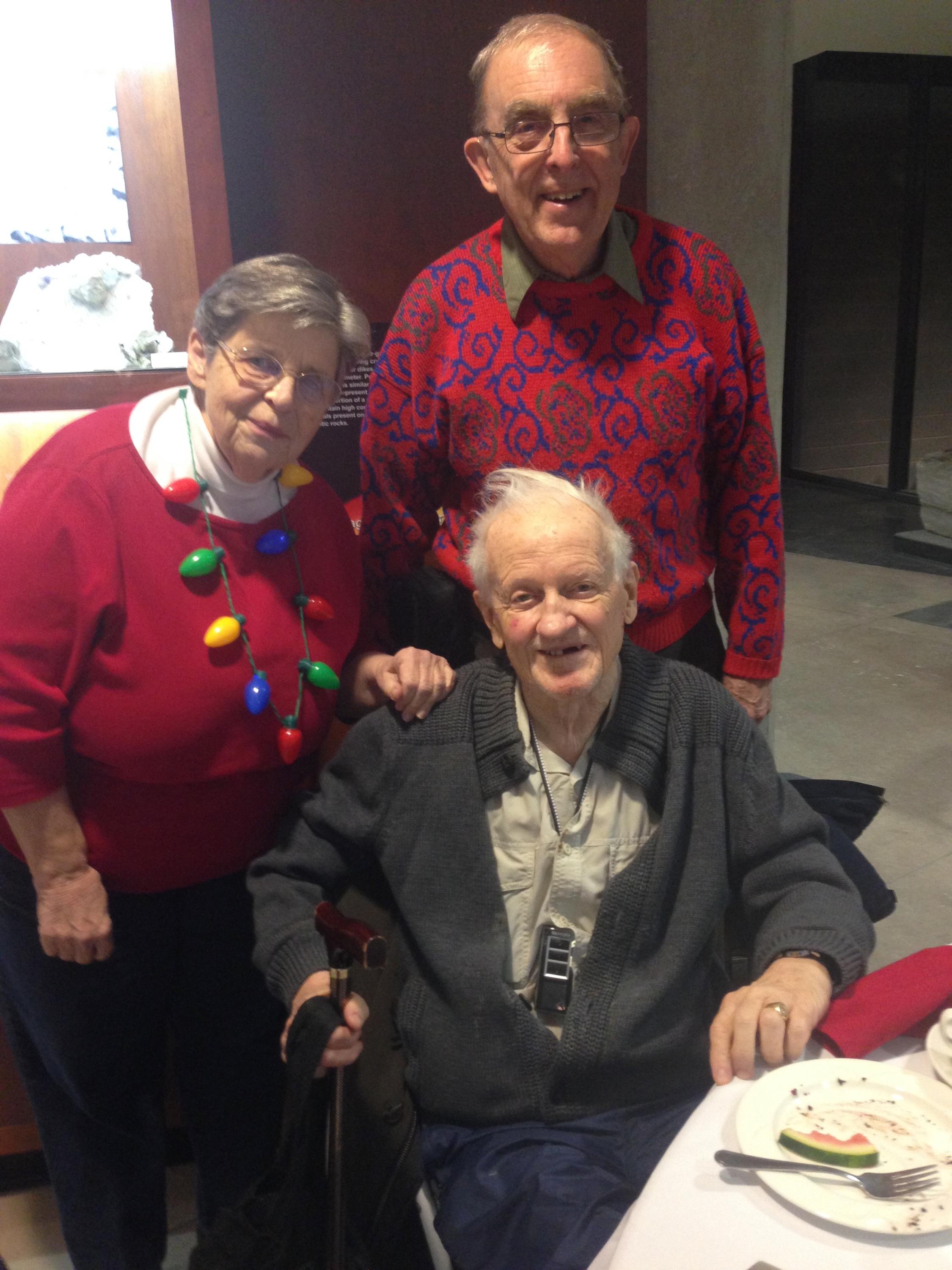 Dr. Frank Brookfield sitting with Peter and Vivian Russell standing behind Frank at the 2017 department Christmas lunch