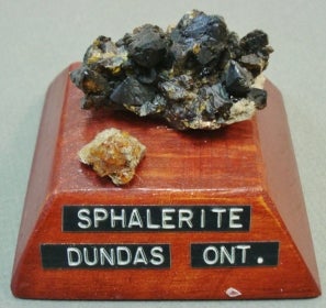 2 pieces of Sphalerite mounted on a wood base with a label; one much larger than the other