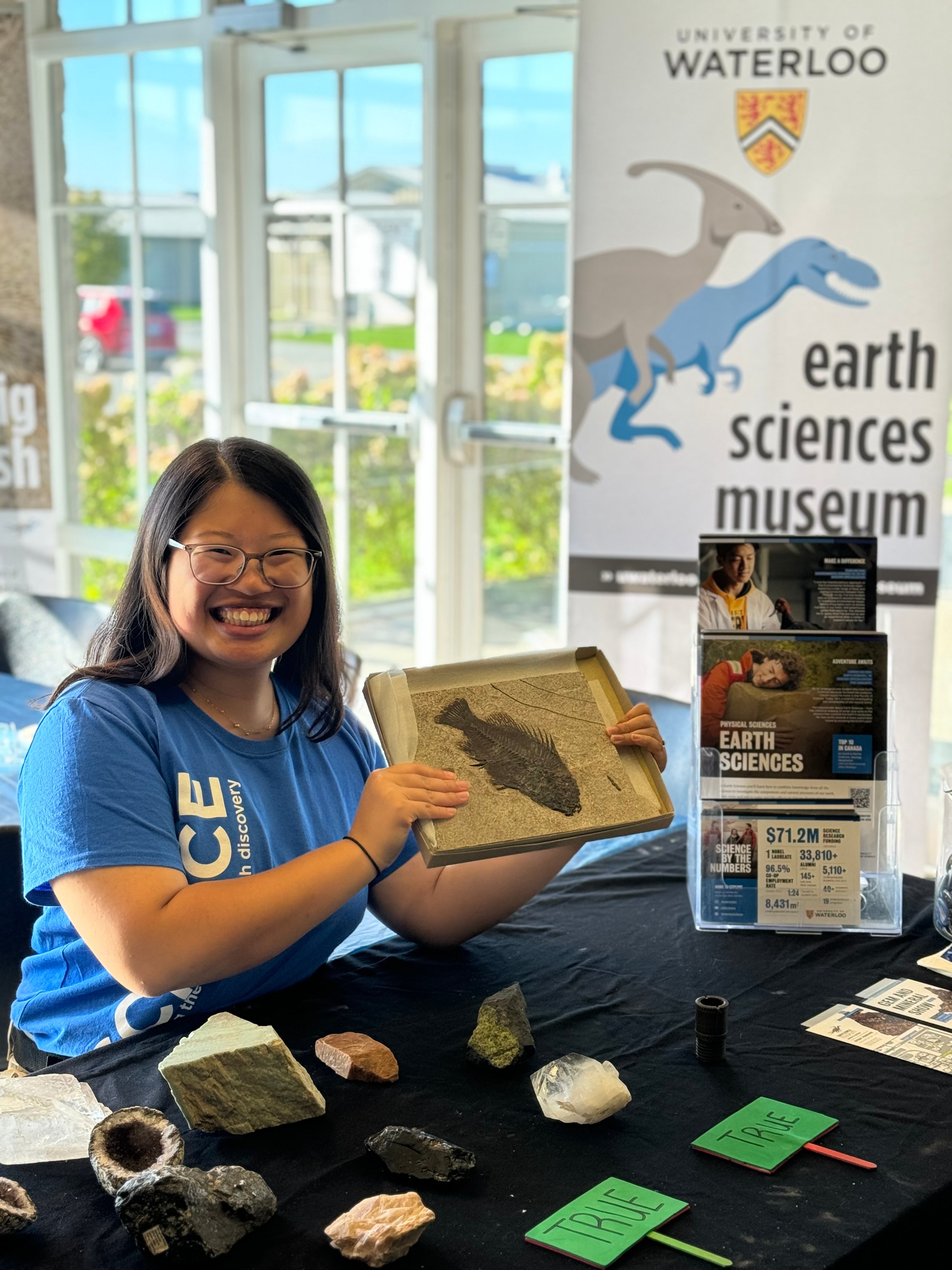 female volunteer at gem show holding up a fossil fish