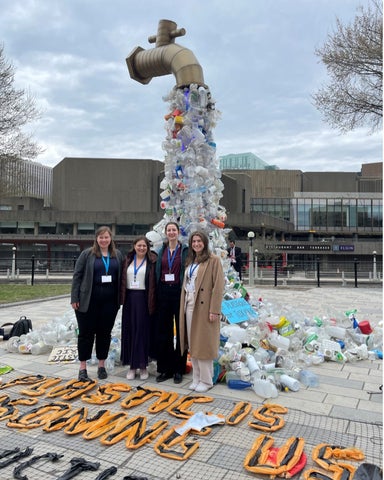 Four members of the Water Institute in front of a sculpture featuring a floating faucet with plastic litter flowing out like water.