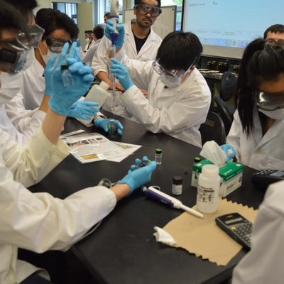 Students in lab coats, gloves and masks doing chemical analysis