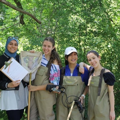 Students in chest waders posing with clipboard, YSI multimeter, and d-net