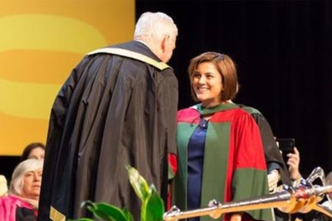 An Economics PhD graduate in academic regalia shakes hands with the University chancellor