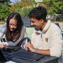two students studying outside using tablets
