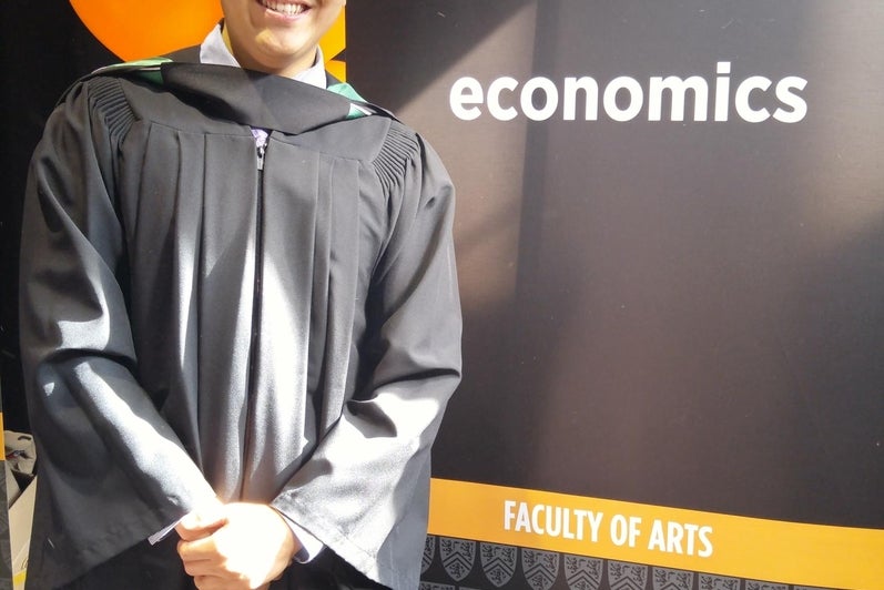 An ECON graduate beside the ECON banner