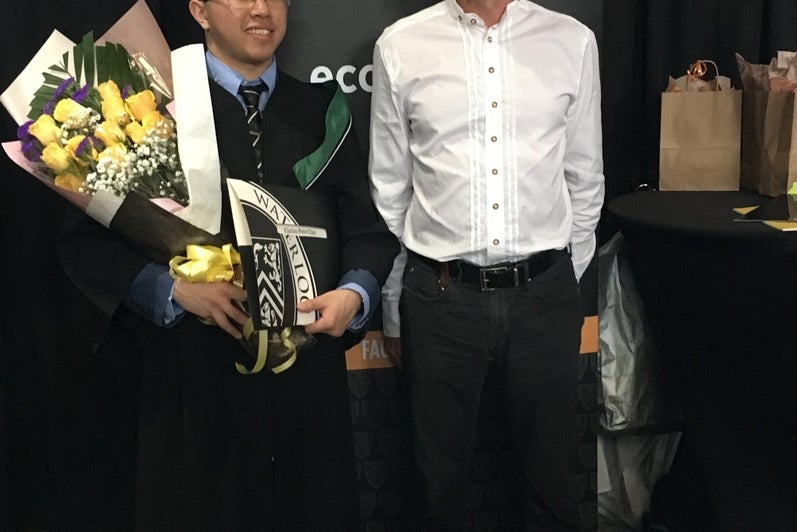 Student holding flowers standing beside a faculty member