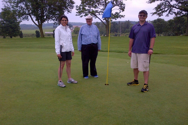 Golfers standing next to the flagstick.