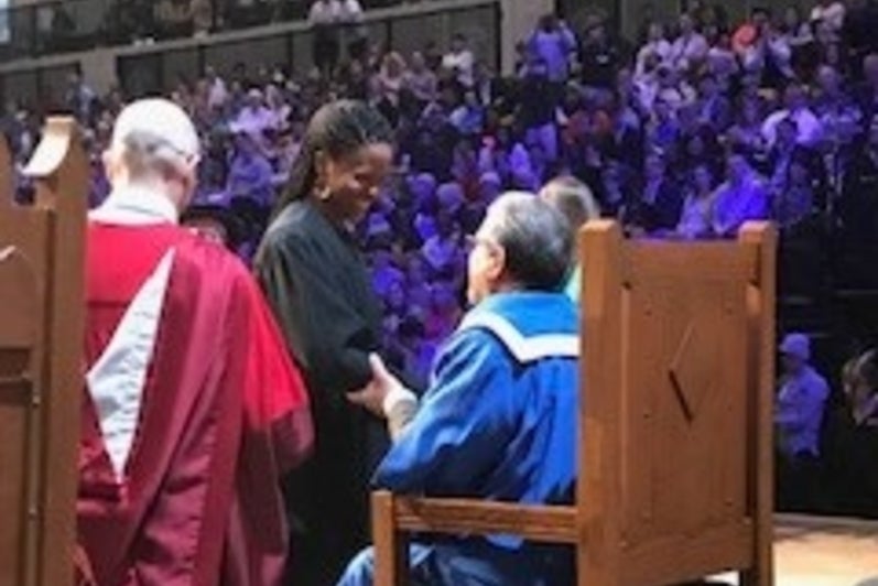 University President sitting in chair shaking hands with a student