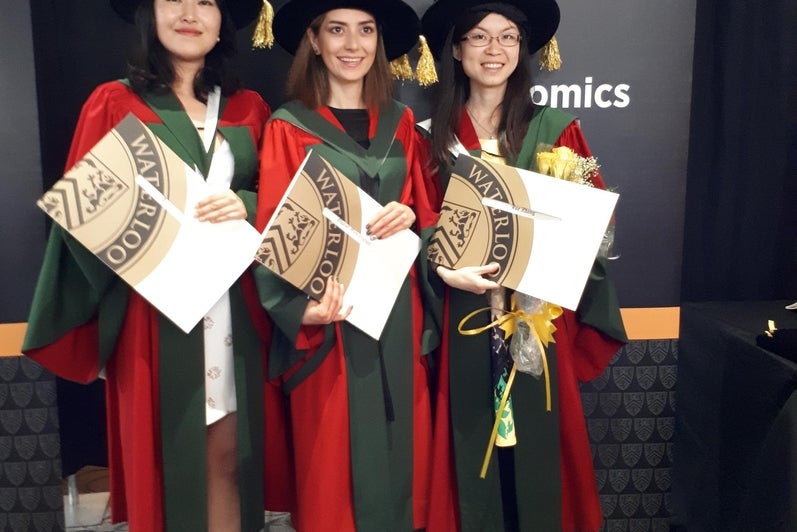 Three PhD graduates holding their degrees