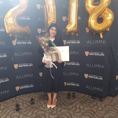 student holding flowers and a degree in front of balloons shaped like 2018