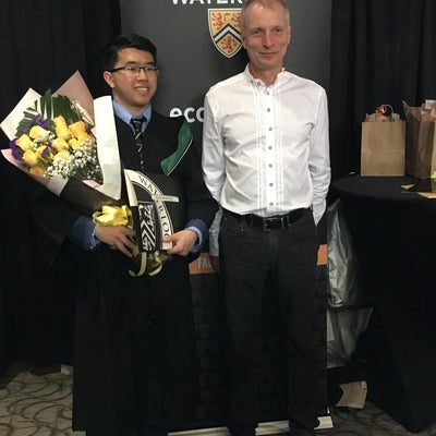 Student holding flowers standing beside a faculty member