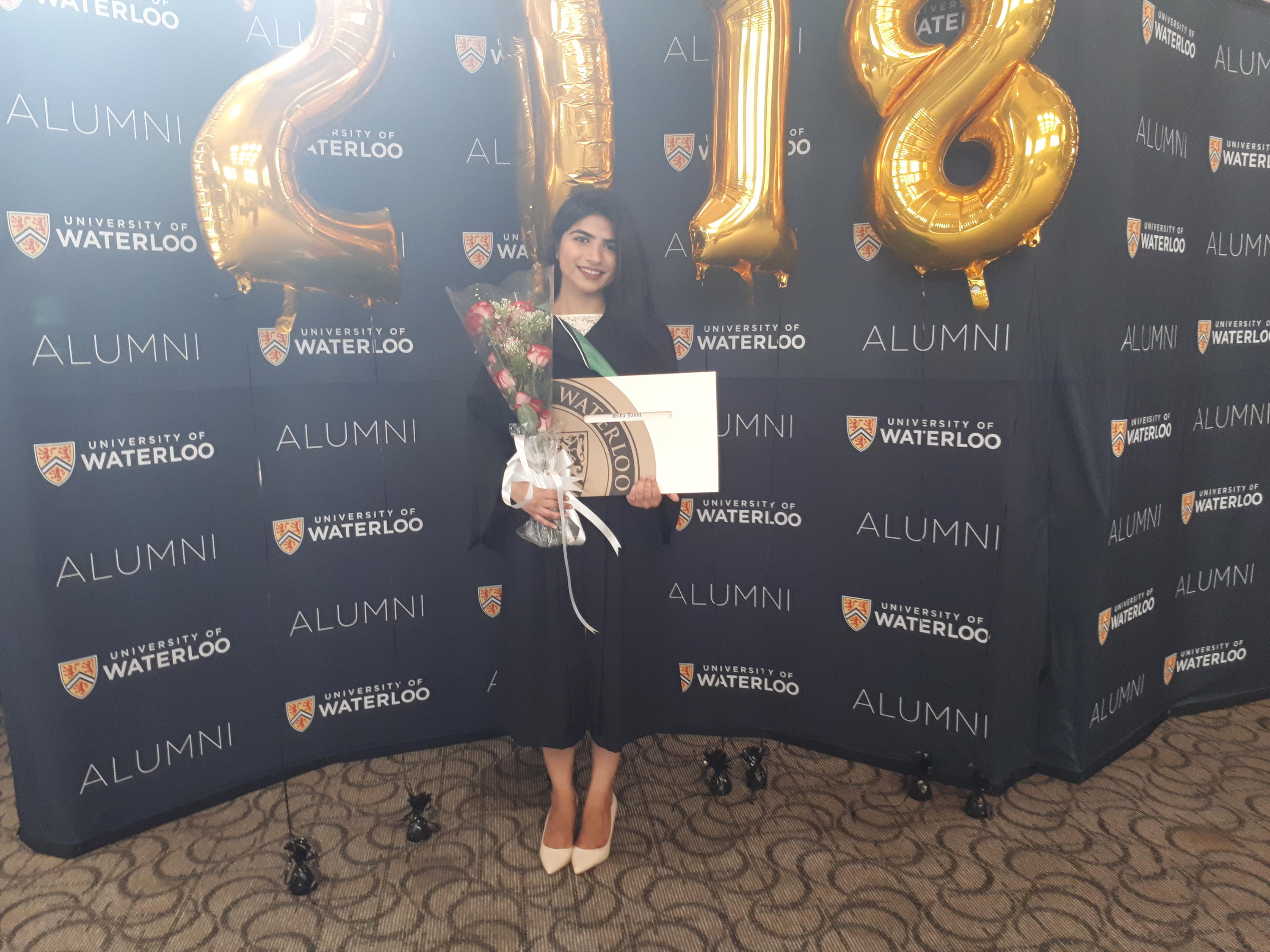 student holding flowers and a degree in front of balloons shaped like 2018