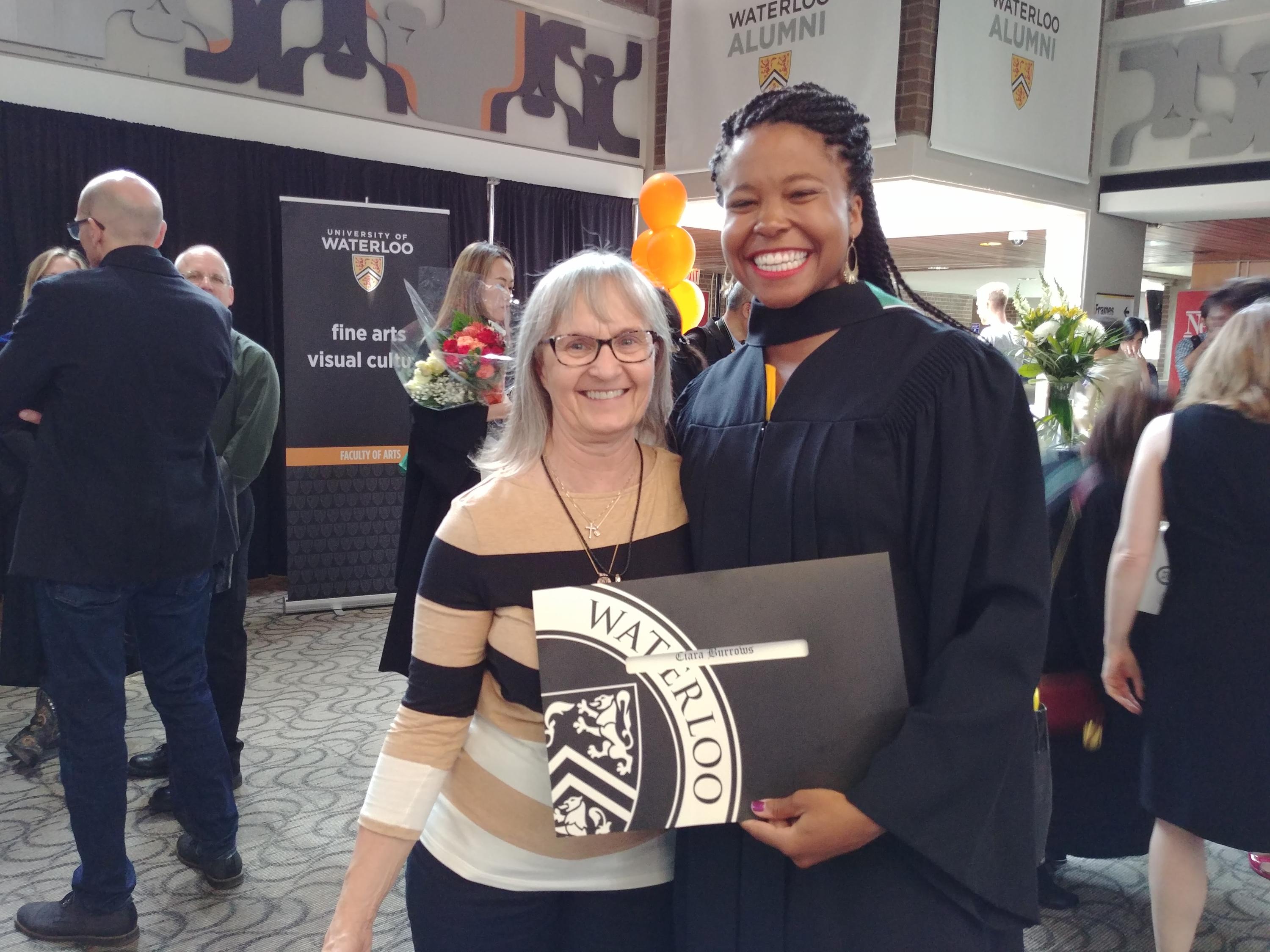 Two women standing beside each other smiling, one holding a diploma