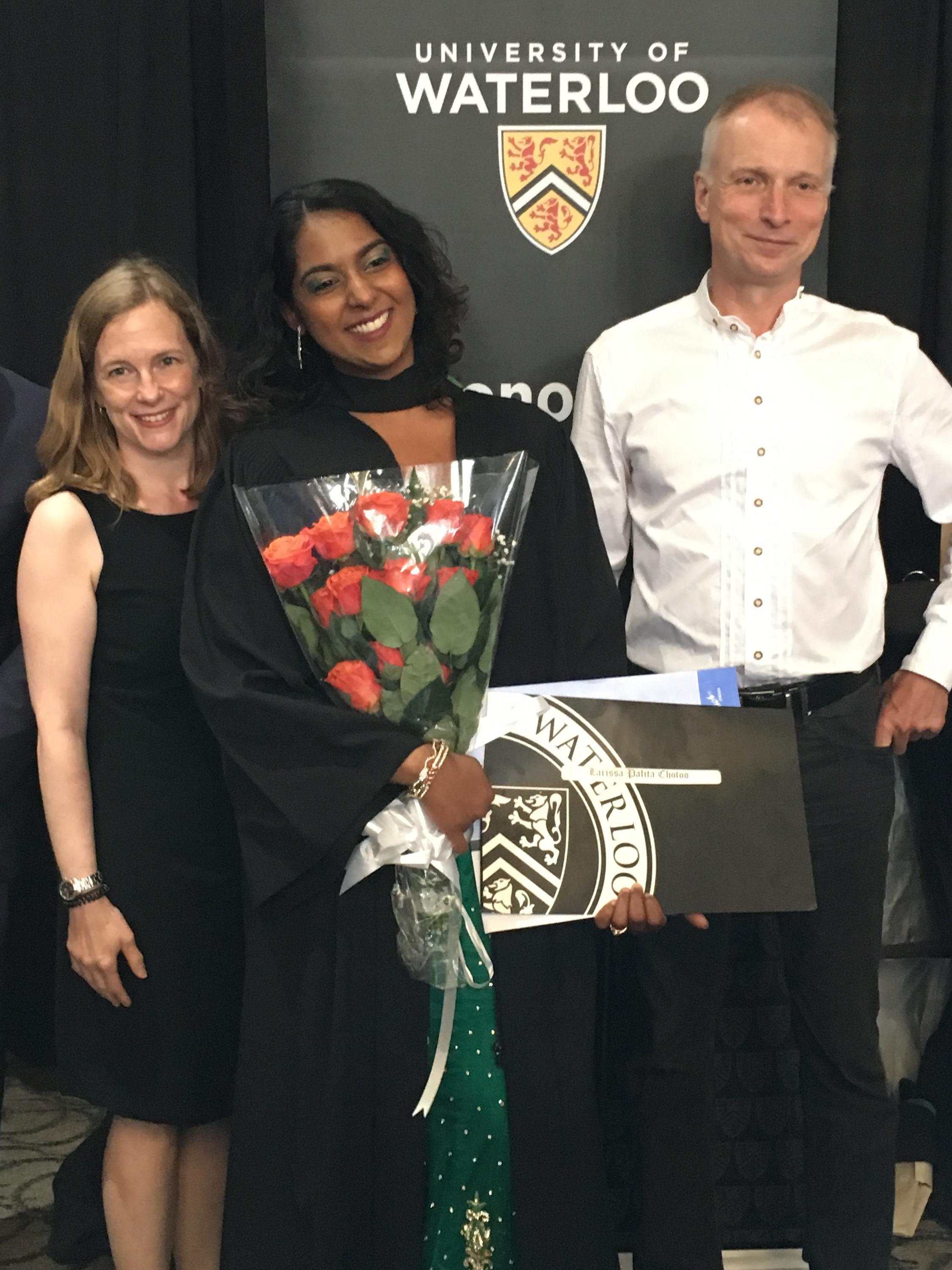 Student holding flowers sandwiched between two faculty members